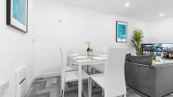A modern living room with a dining area, white furniture, a grey sofa, and a television displaying a movie.