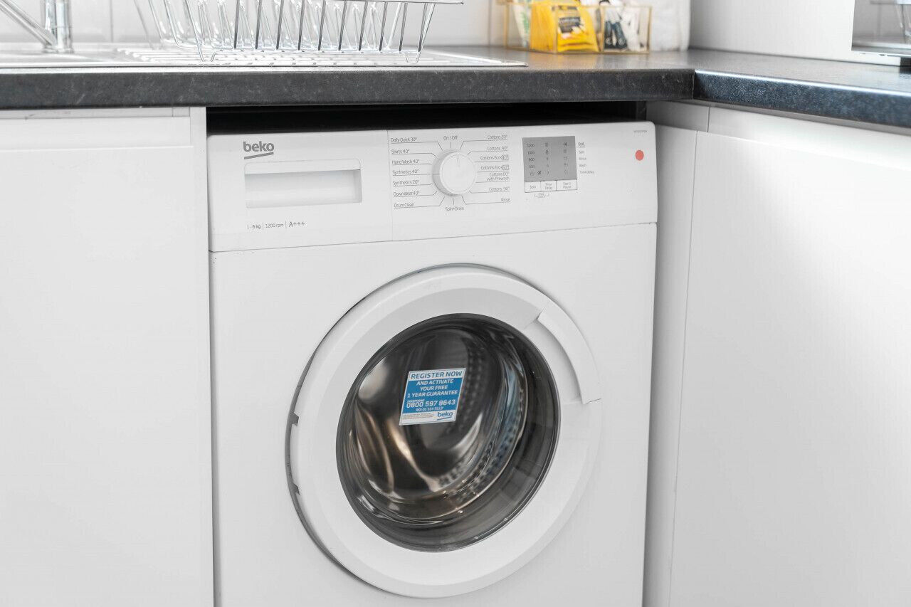 A front view of a modern, white washing machine with a control panel and a label on the door.