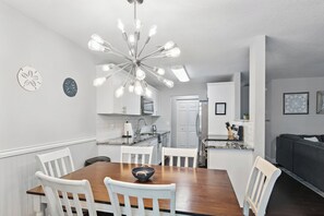 A modern kitchen with white cabinetry, a wooden dining table, and a unique light fixture. - Paradise Bliss! Heated Pool, Near Boat Ramp, Beaches, & Golf Course,Wifi (Sebastian)