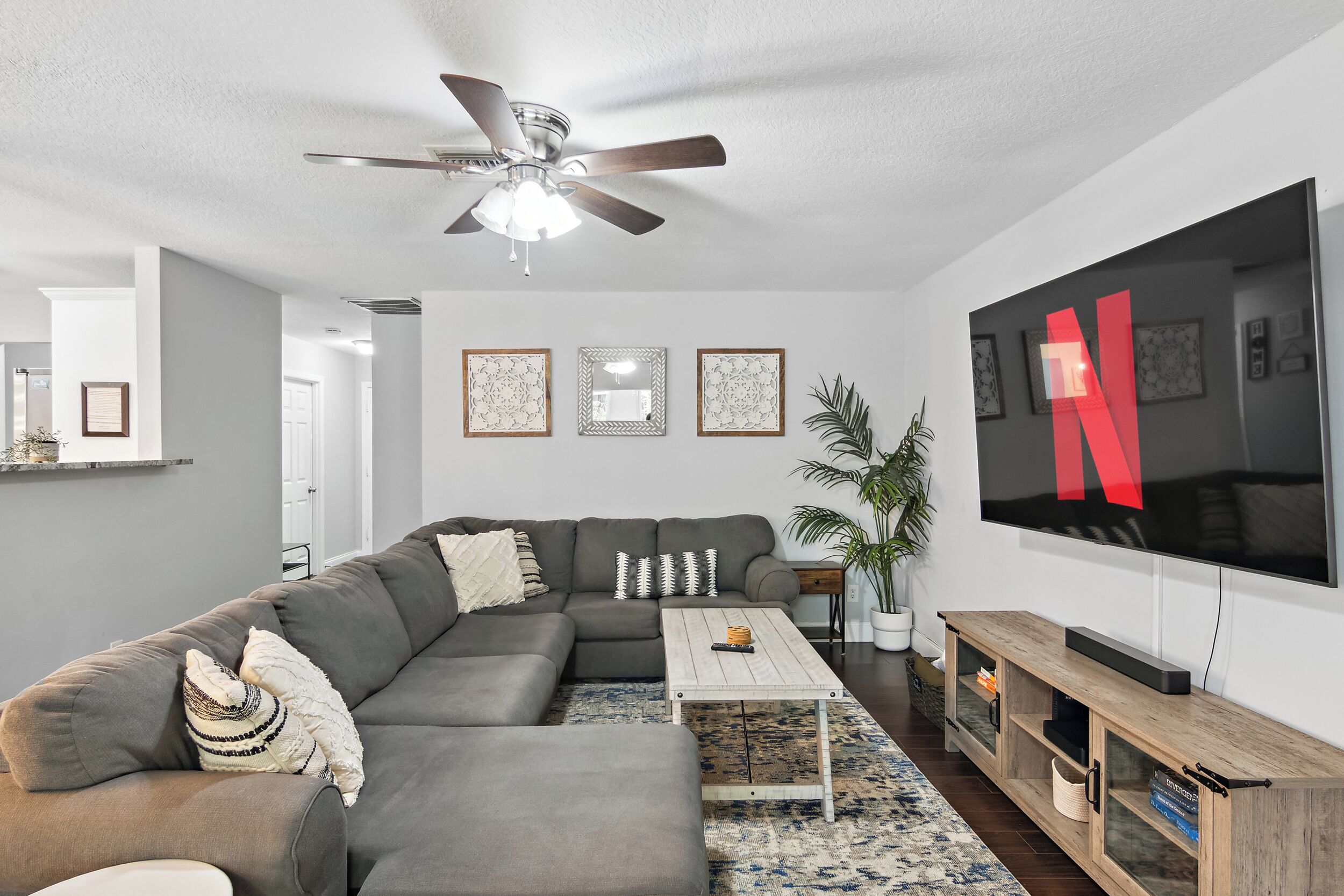 Un salon moderne avec un canapé d’angle, un ventilateur de plafond, un téléviseur à écran plat et une table basse en bois.