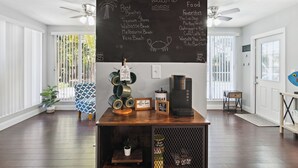 A room with a wooden floor, a coffee bar with a chalkboard menu, ceiling fans, and a view of the outdoors.