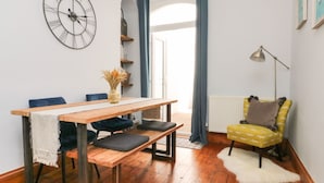 Ein modernes Wohnzimmer mit einem Holzesstisch, blauen Stühlen, einem gelben Sessel, einer großen Wanduhr und einer Stehlampe.