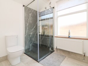 A modern bathroom with a glass shower enclosure, a white toilet, and a window with a view. - Torrs Walk View (Ilfracombe)