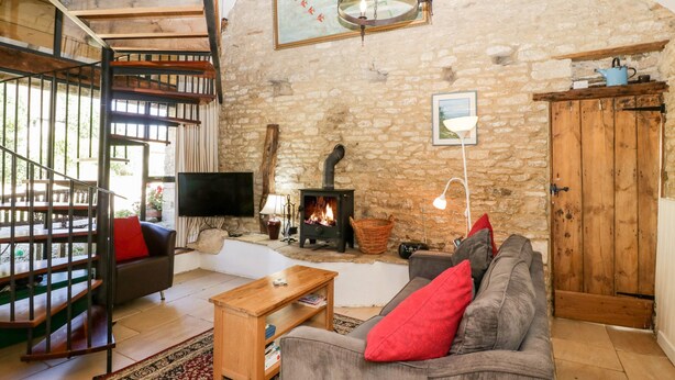 Ein rustikales Wohnzimmer mit Steinwand, Kamin, einer Holztreppe und einem Fernseher.