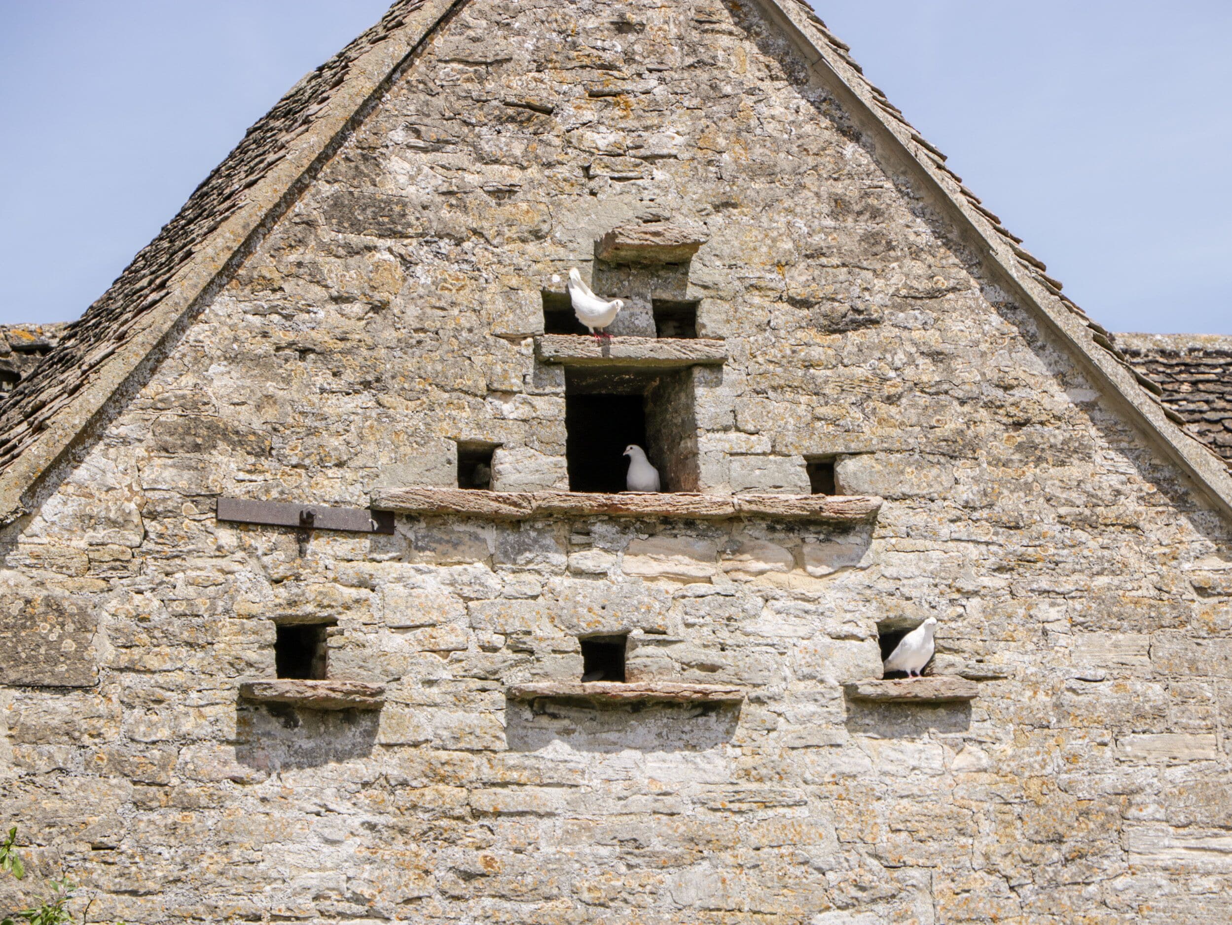 Ein Steinhaus mit mehreren kleinen Fenstern und einem größeren, zentralen Fenster, auf dessen Sims ein Vogel sitzt.