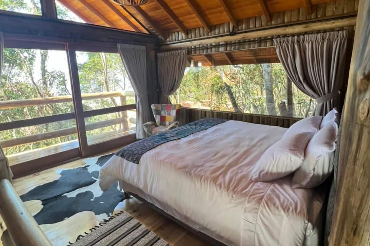 A wooden cabin bedroom with a bed, curtains, and a hanging light fixture.