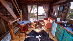 A rustic cabin interior with a wooden dining table, a sofa, a kitchen area, and a large cowhide rug. - Pousada Parador 33 (Biguacu)