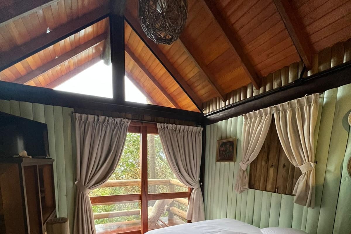 A cozy bedroom with a large bed, wooden ceiling, and a view of the outdoors through a window.
