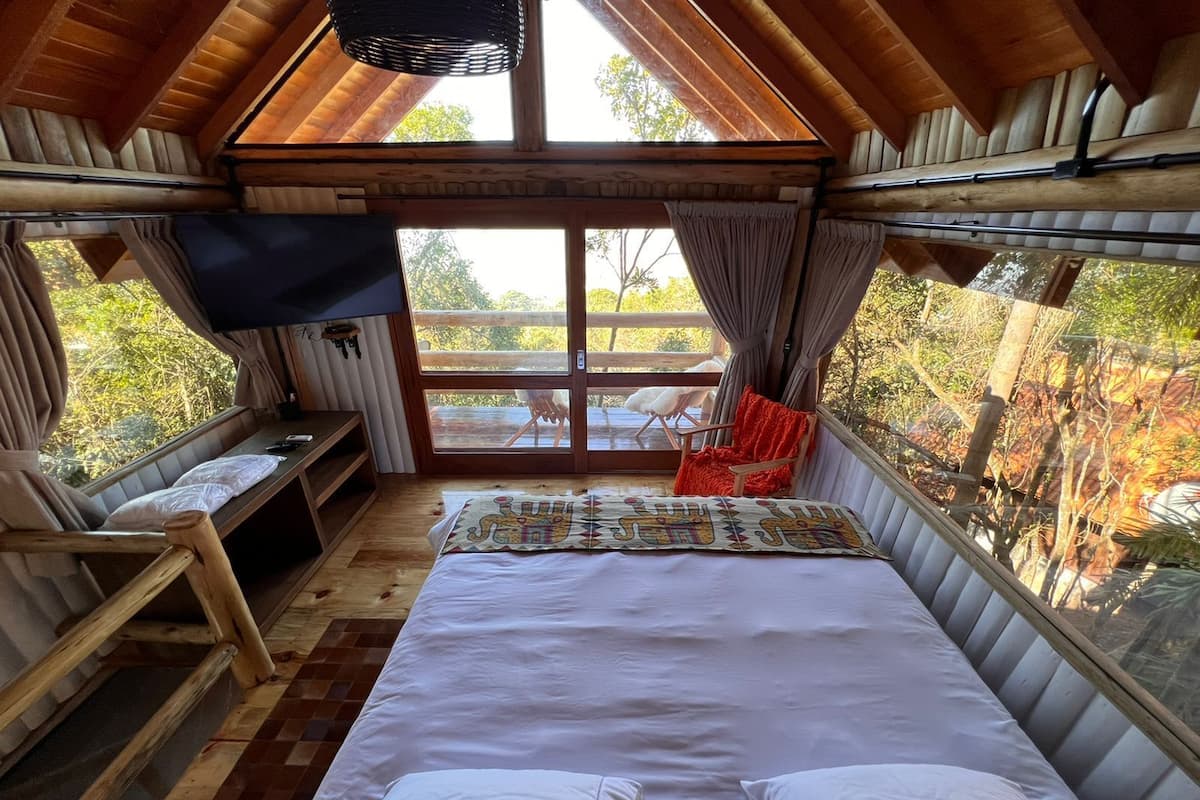 A cozy room with a bed, a TV, a bench, and a window overlooking a deck.