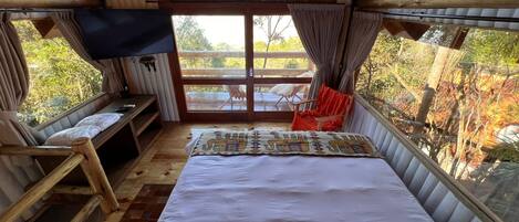 A cozy room with a bed, a TV, a bench, and a window overlooking a deck.