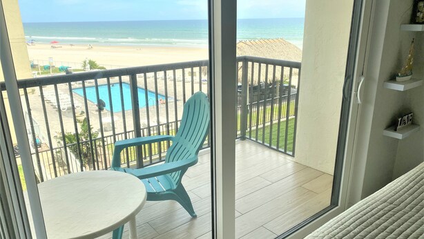 Un balcon avec vue sur la plage, une piscine et une chaise bleue.