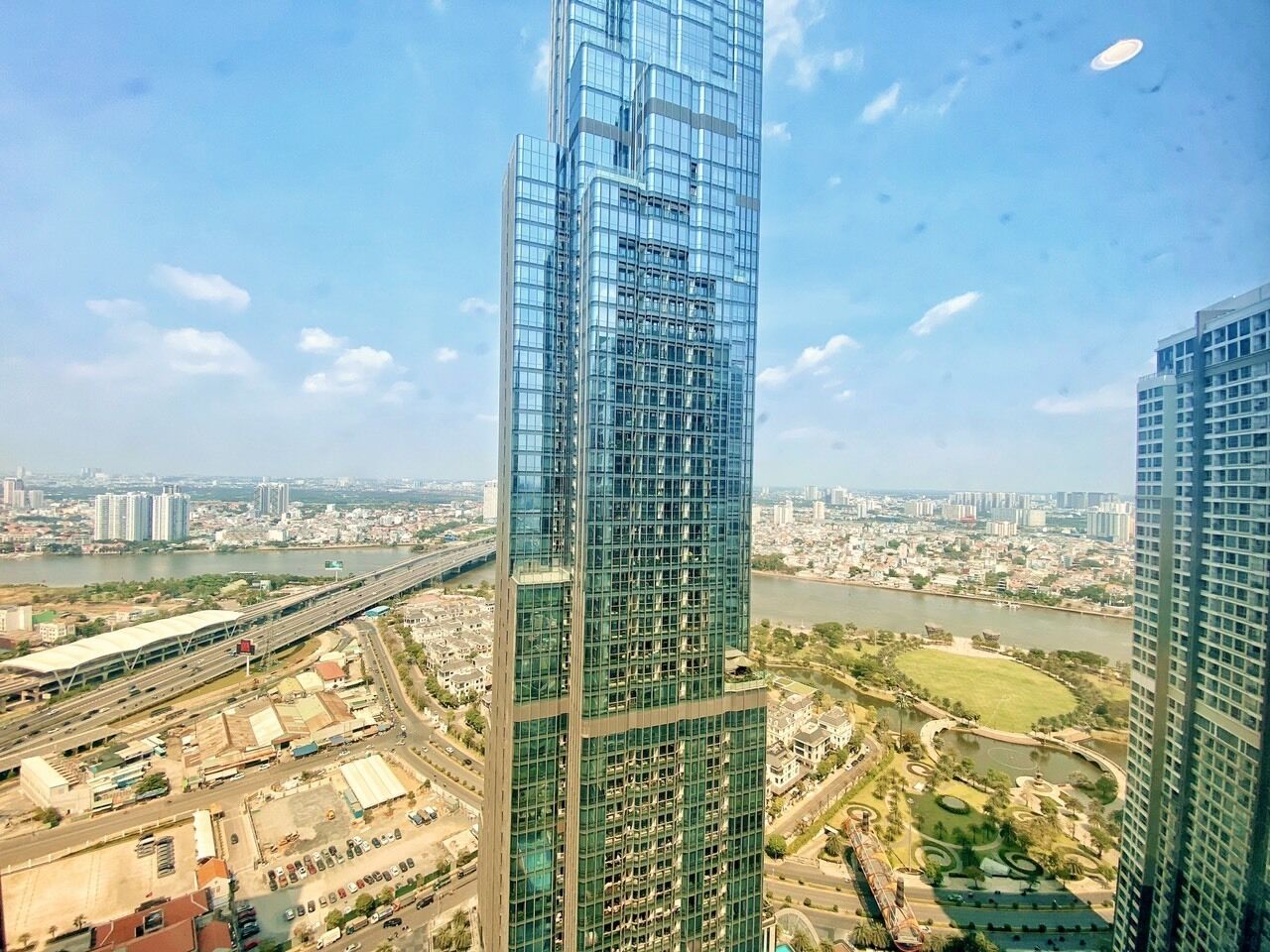 Un immeuble de grande hauteur à la façade en verre, entouré d’un paysage urbain et bordé par une rivière.