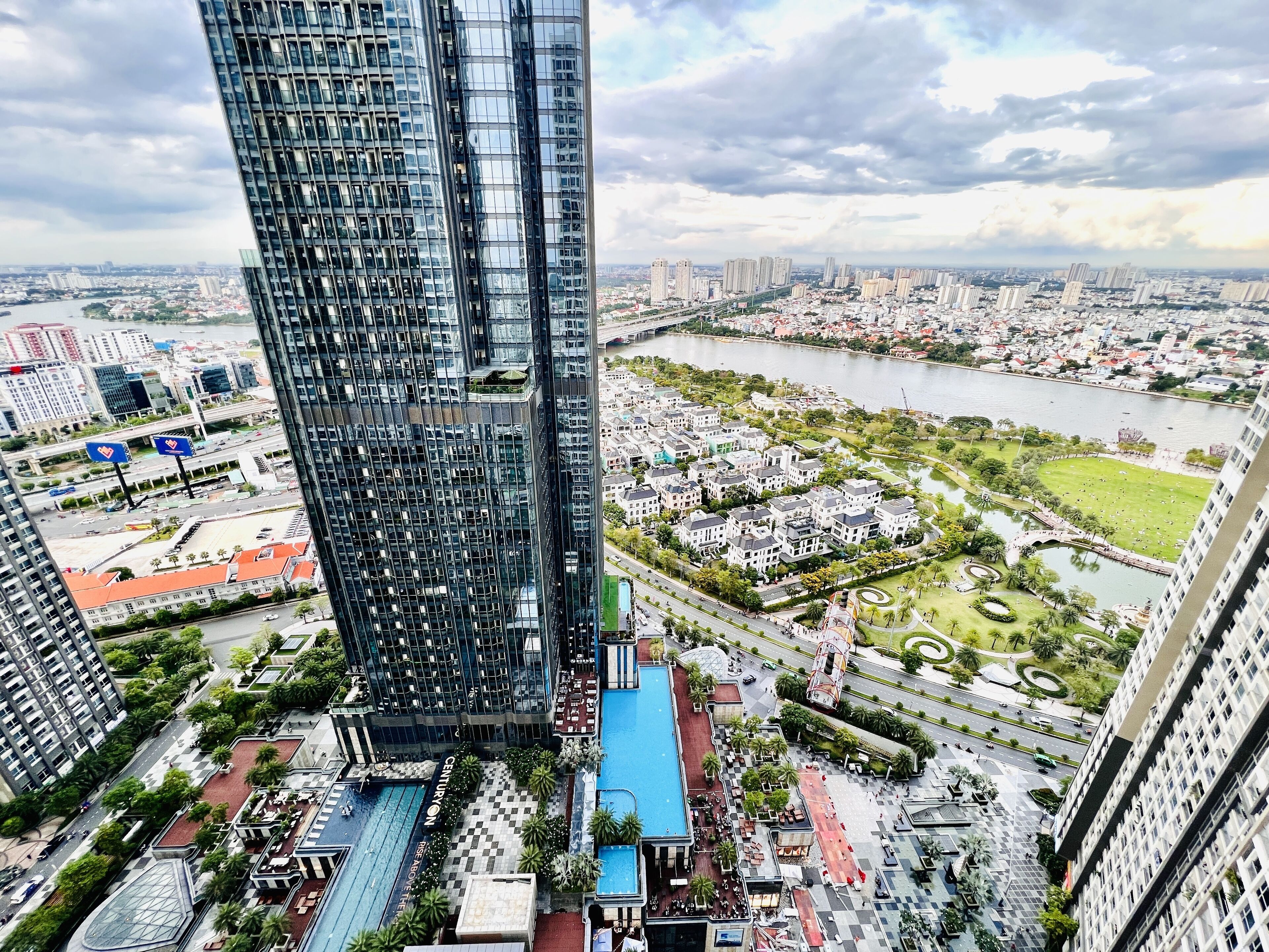 Un immeuble de grande hauteur doté d’une façade moderne en verre, d’une piscine et d’un espace paysager offrant une vue sur la rivière.