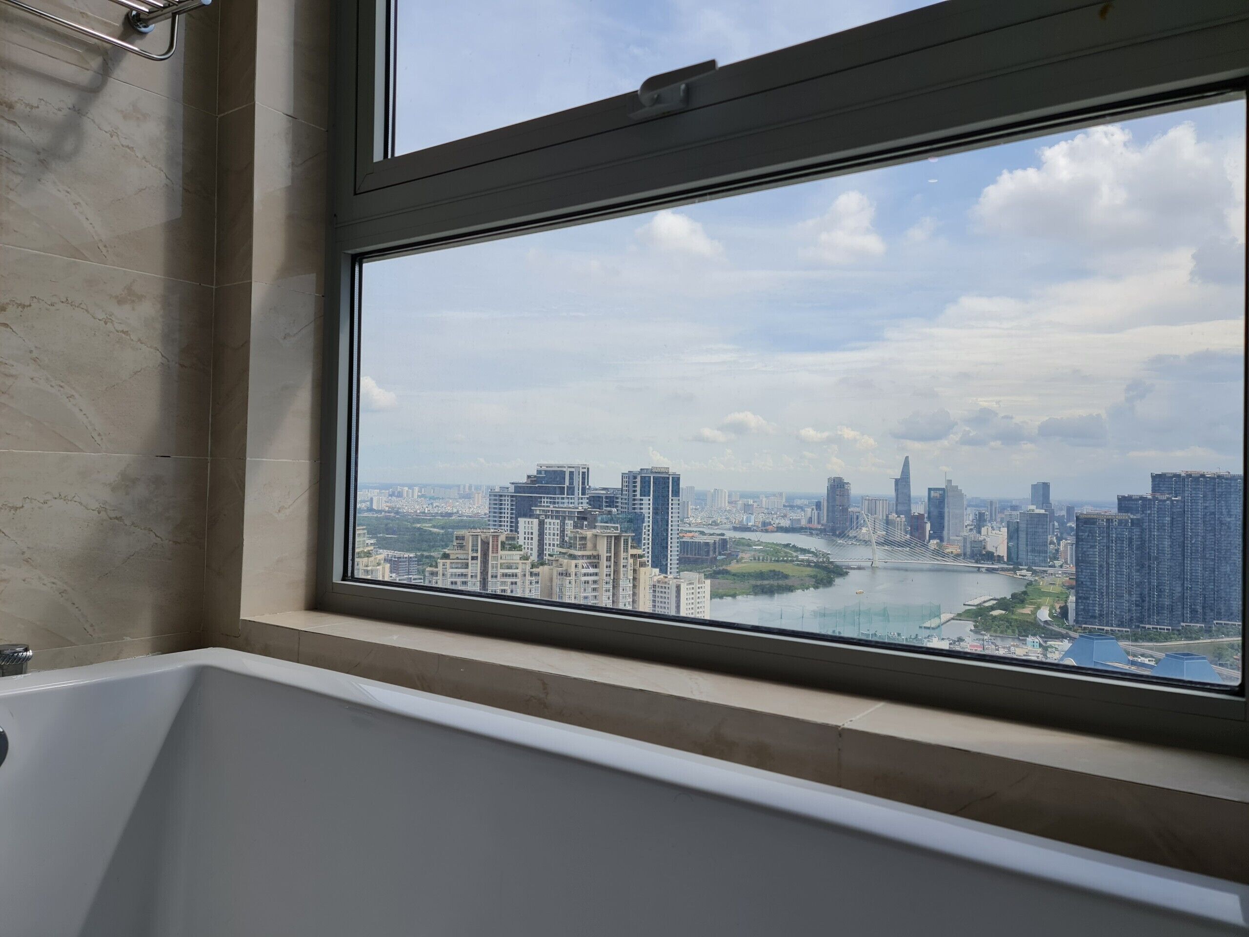 A bathroom with a bathtub and a large window overlooking a cityscape with buildings and a river.