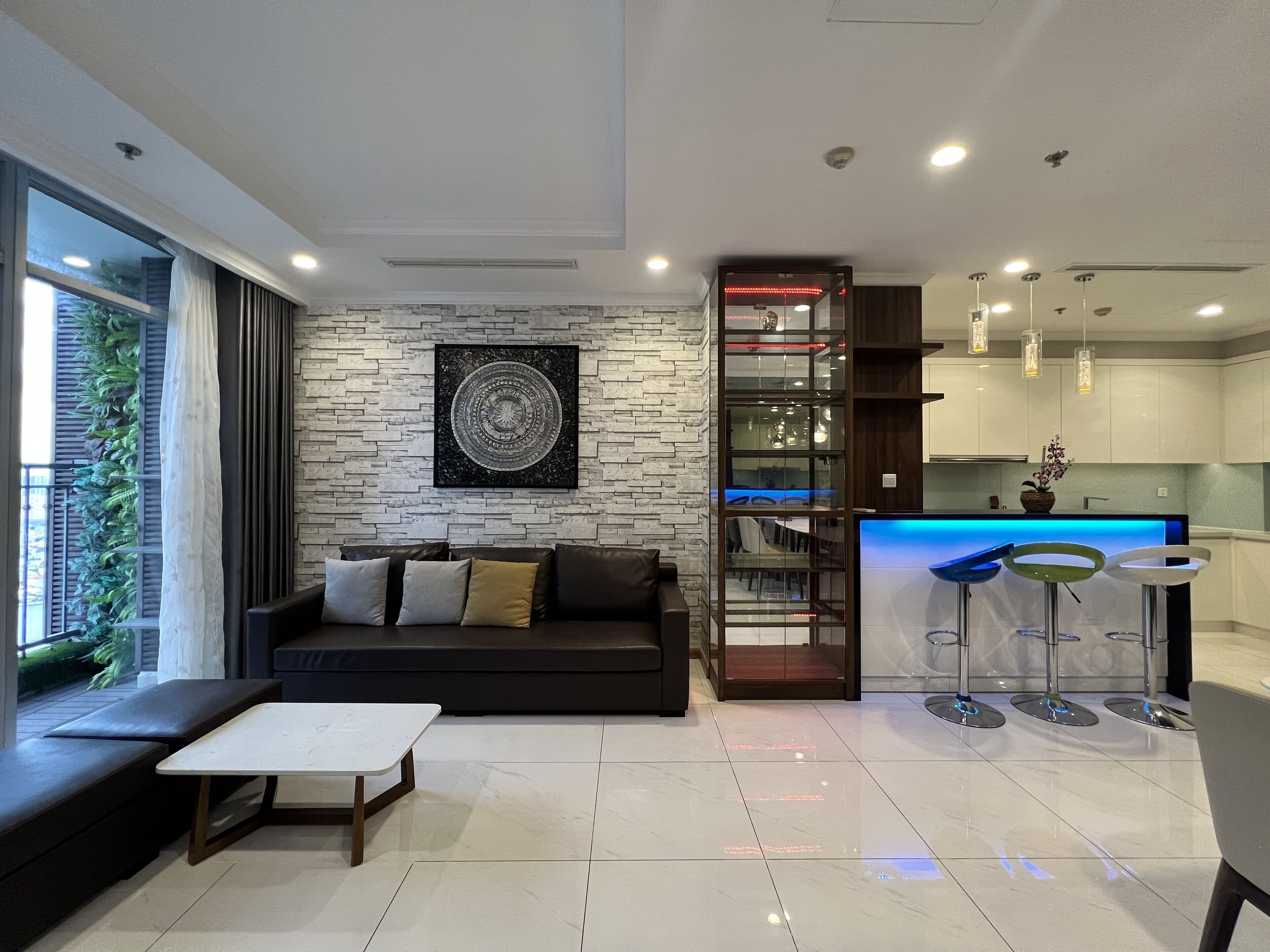 Un salon moderne avec un canapé noir, une table basse blanche et un mur décoré d’un motif imitant la pierre.