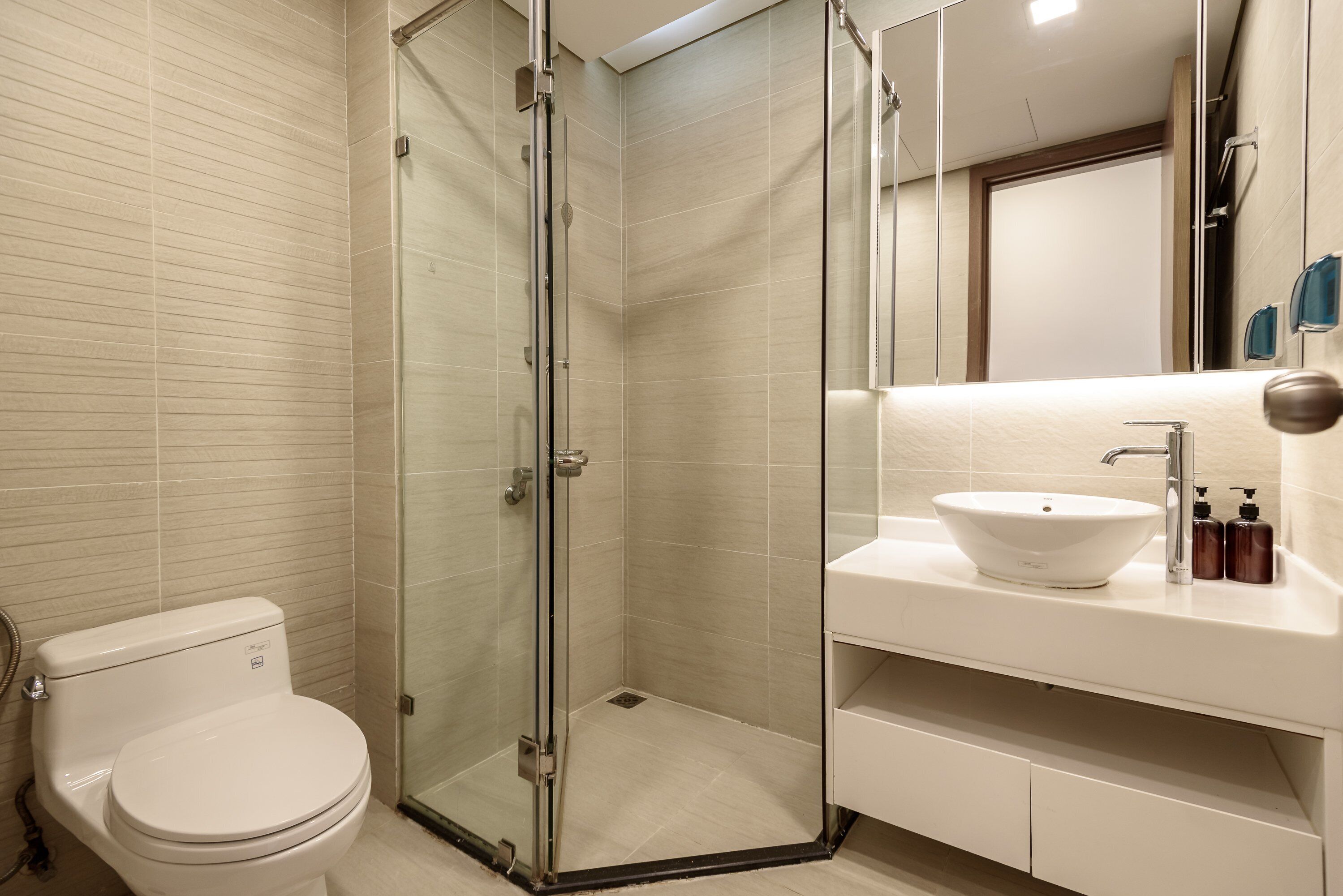 A modern bathroom with a glass-enclosed shower, a white sink, and a toilet.