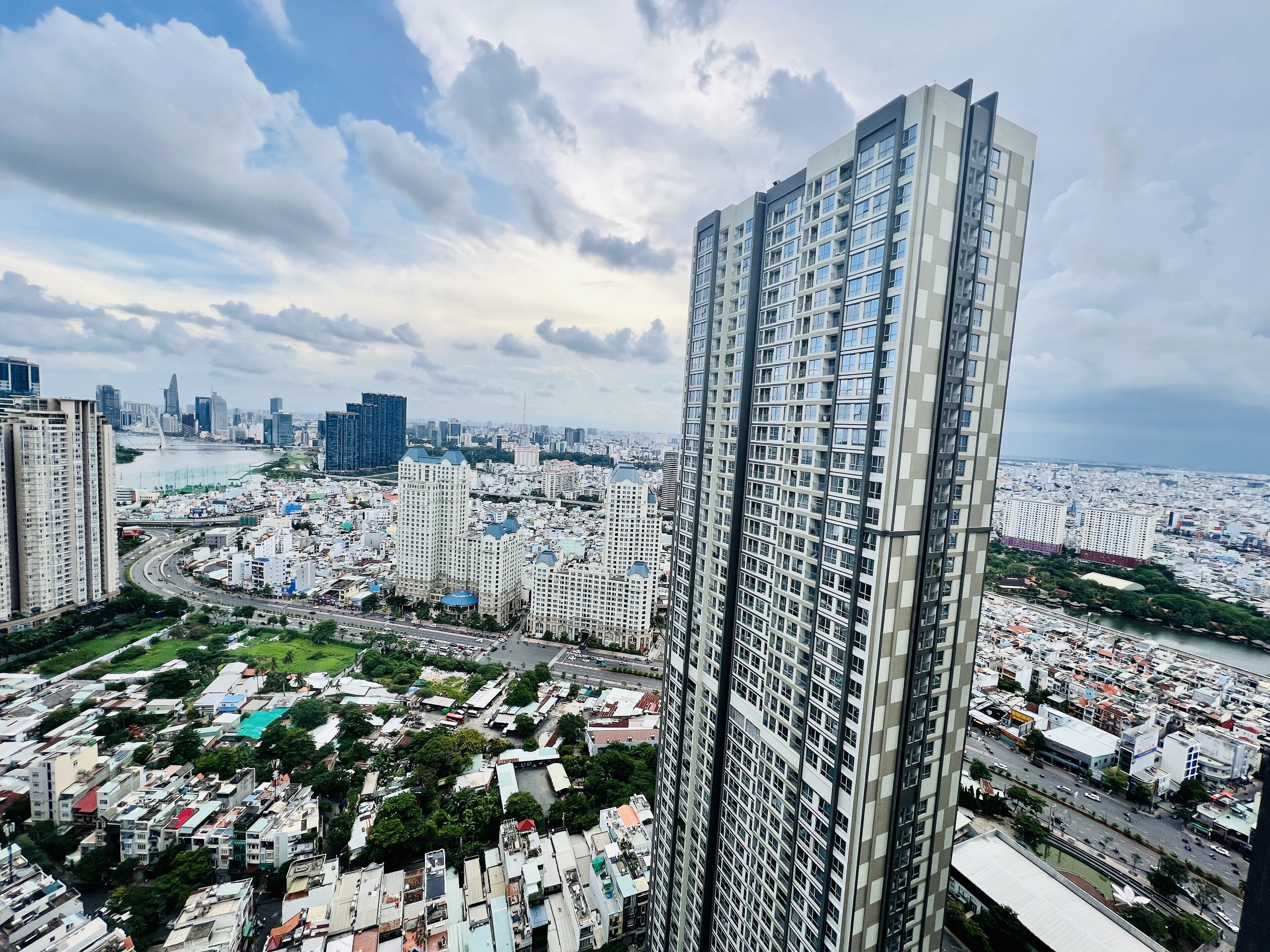 A high-rise building with a modern architectural design, surrounded by a dense urban area with various buildings and a river in the background.