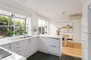 A modern kitchen with white cabinets, a built-in dishwasher, and a large window overlooking greenery.