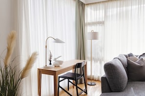 A modern living room with a wooden table, a black chair, a floor lamp, and a sofa.