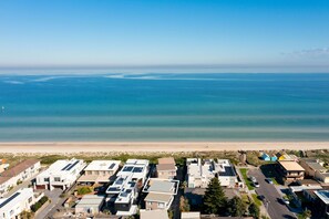 An aerial view of a coastal residential area with houses, a beach, and a clear view of the ocean.