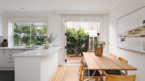 Une cuisine moderne dotée d’un grand îlot central, d’un coin repas avec des meubles en bois et offrant une vue sur un jardin et un espace extérieur.