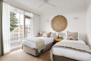 A bedroom with two beds, a ceiling fan, a large woven wall art piece, and a view of the outdoors through a sliding door.