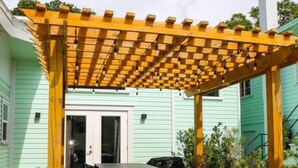 A wooden pergola with a table and chairs underneath, surrounded by plants and a brick pathway. - The Euclid 1925 Bungalow Located in Downtown (St. Petersburg)