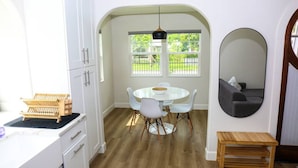 A modern kitchen with white cabinets, a round dining table with white chairs, and a wooden bench. - The Euclid 1925 Bungalow Located in Downtown (St. Petersburg)