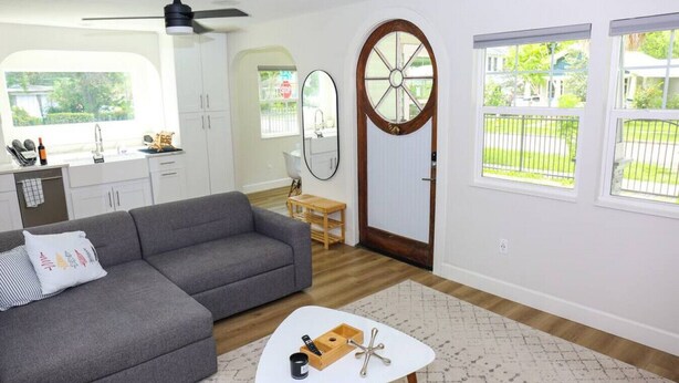 A modern living room with a grey sofa, a small white coffee table, and a wooden door with a window. - The Euclid 1925 Bungalow Located in Downtown (St. Petersburg)
