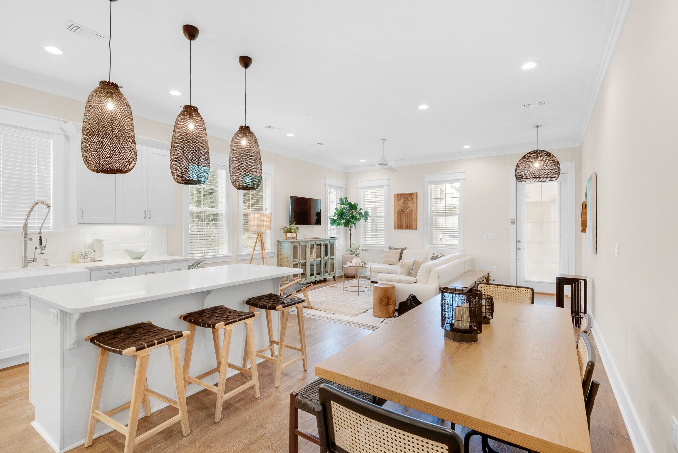 A modern kitchen with a central island, bar stools, pendant lighting, and a dining area with a wooden table and chairs.