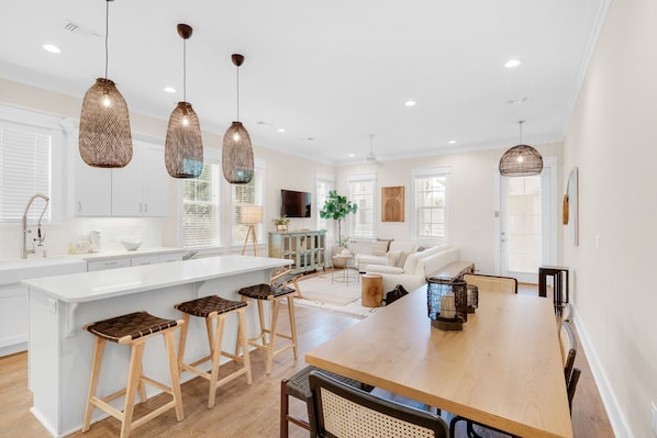 A modern kitchen with a central island, bar stools, pendant lighting, and a dining area with a wooden table and chairs. - ☀️Spacious Balcony-Luxury 30A-Bikes-Pool-Grayton 91 (Santa Rosa Beach)