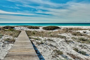 A wooden boardwalk leading to a beach with clear skies and calm waters.