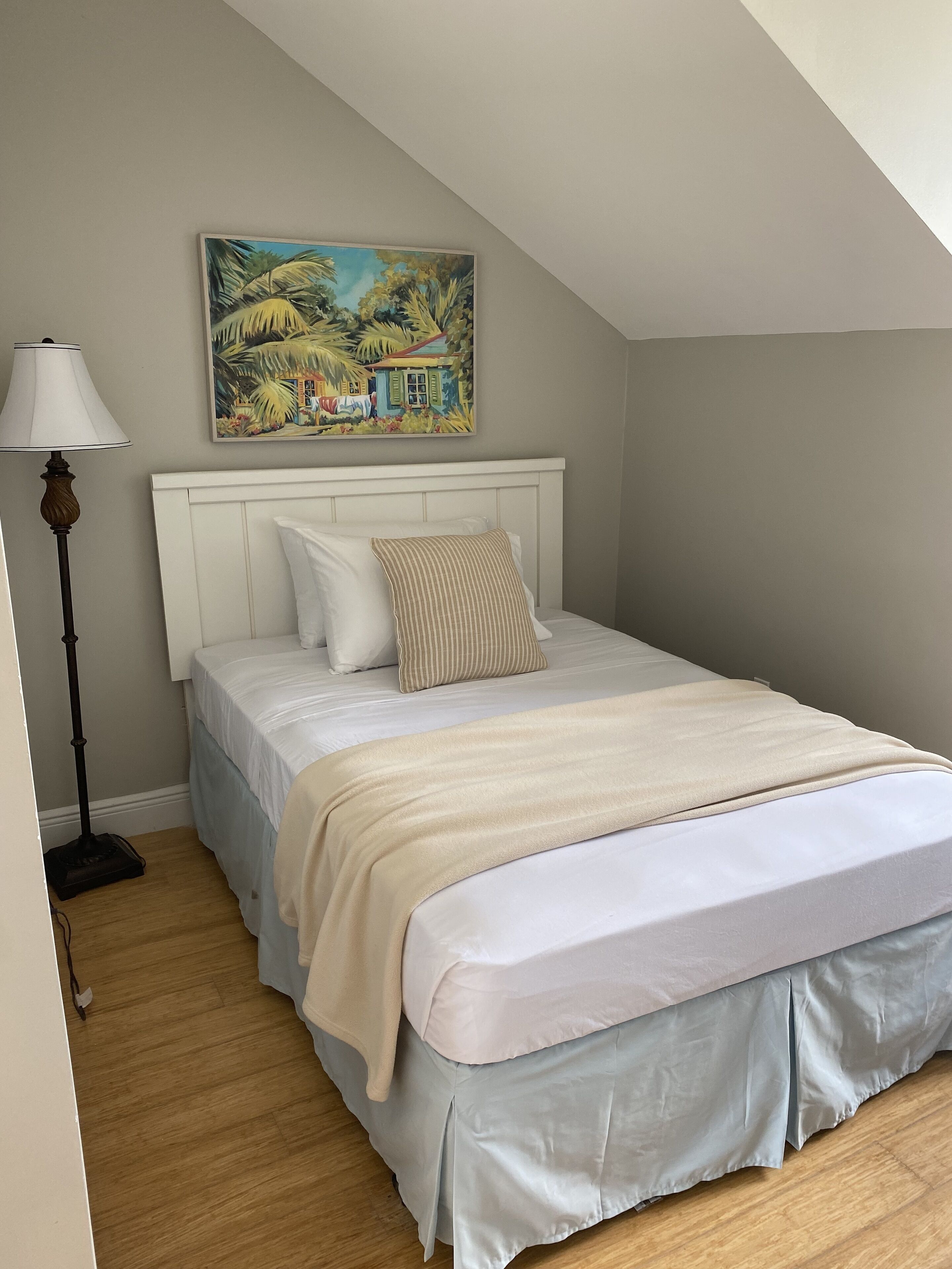 Ein Schlafzimmer mit einem Bett, einem Gemälde darüber und einer Stehlampe.