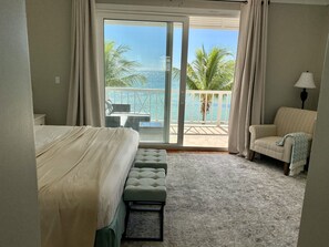Une chambre d’hôtel avec un lit, une chaise, une petite table et une vue sur l’océan par une porte coulissante.