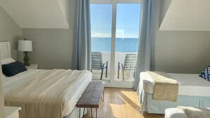 Camera d'albergo con due letti, un tavolino, una lampada e vista sul mare attraverso una porta vetrata.