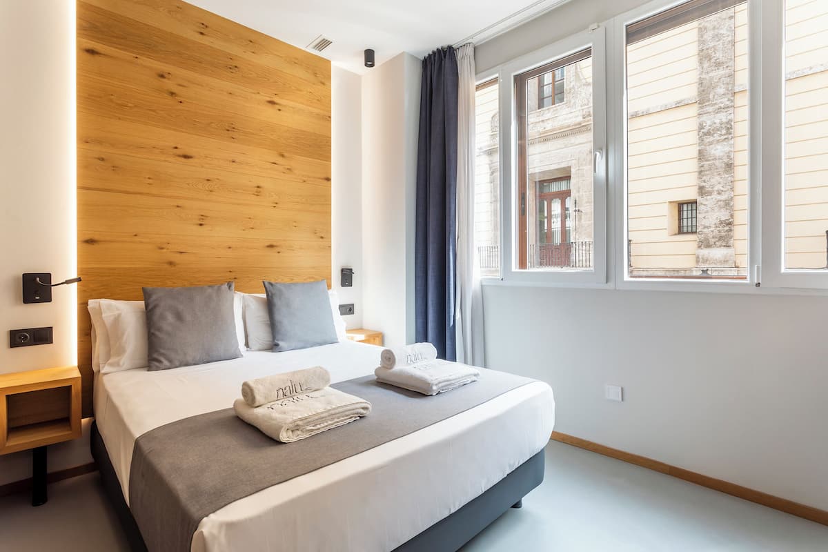 A modern hotel room with a large bed, wooden headboard, and a view of a building through the window.