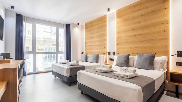 A modern hotel room with two beds, a wooden accent wall, a large window, and a desk. - Nalu Valencia Boutique Rooms (Valencia)