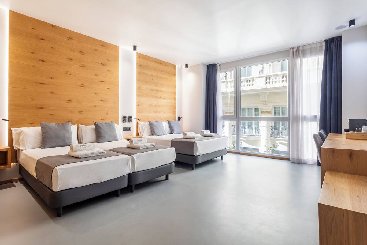 A modern hotel room with a large bed, a smaller bed, a desk, and a balcony view.