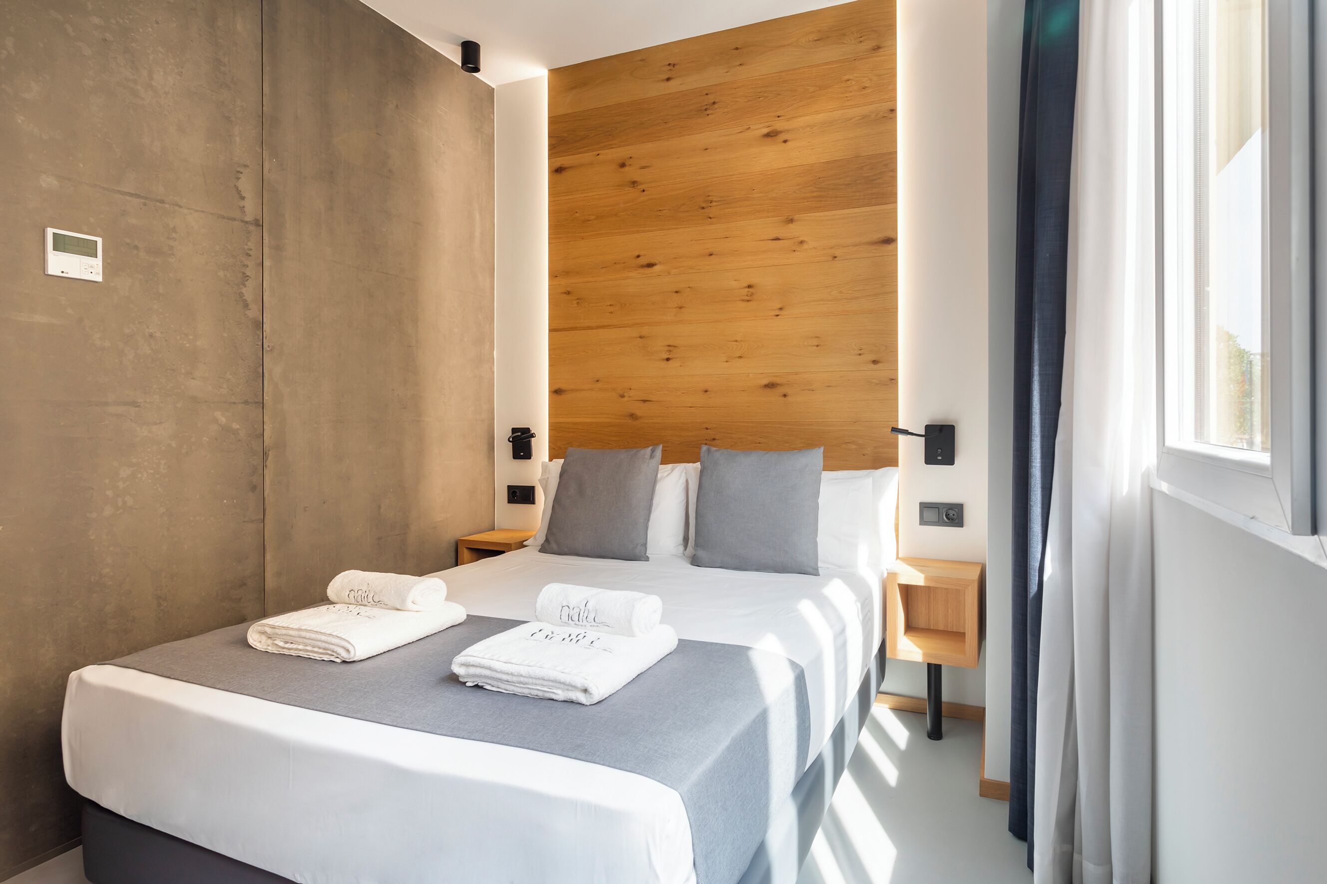 Una habitación de hotel moderna con una cama grande, cabecera de madera y una mesita de noche pequeña.