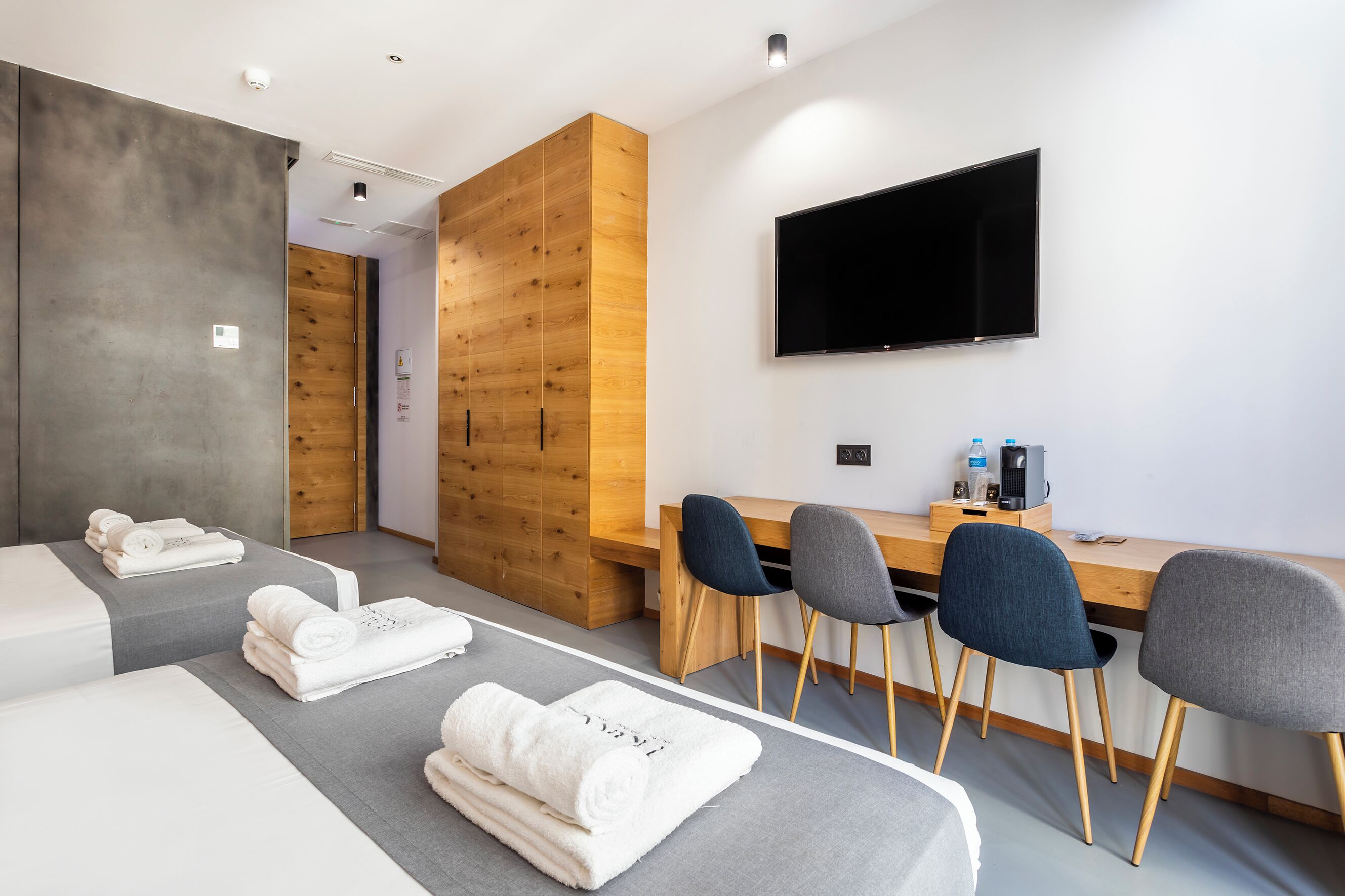 Una habitación de hotel moderna con una cama grande, un escritorio con sillas, un televisor de pantalla plana y un armario de madera.