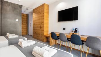 Una habitación de hotel moderna con una cama grande, un escritorio con sillas, un televisor de pantalla plana y un armario de madera.