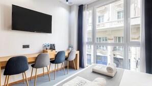 A hotel room with a bed, a desk with chairs, a flat-screen TV, and a large window with a view of a building. - Nalu Valencia Boutique Rooms (Valencia)