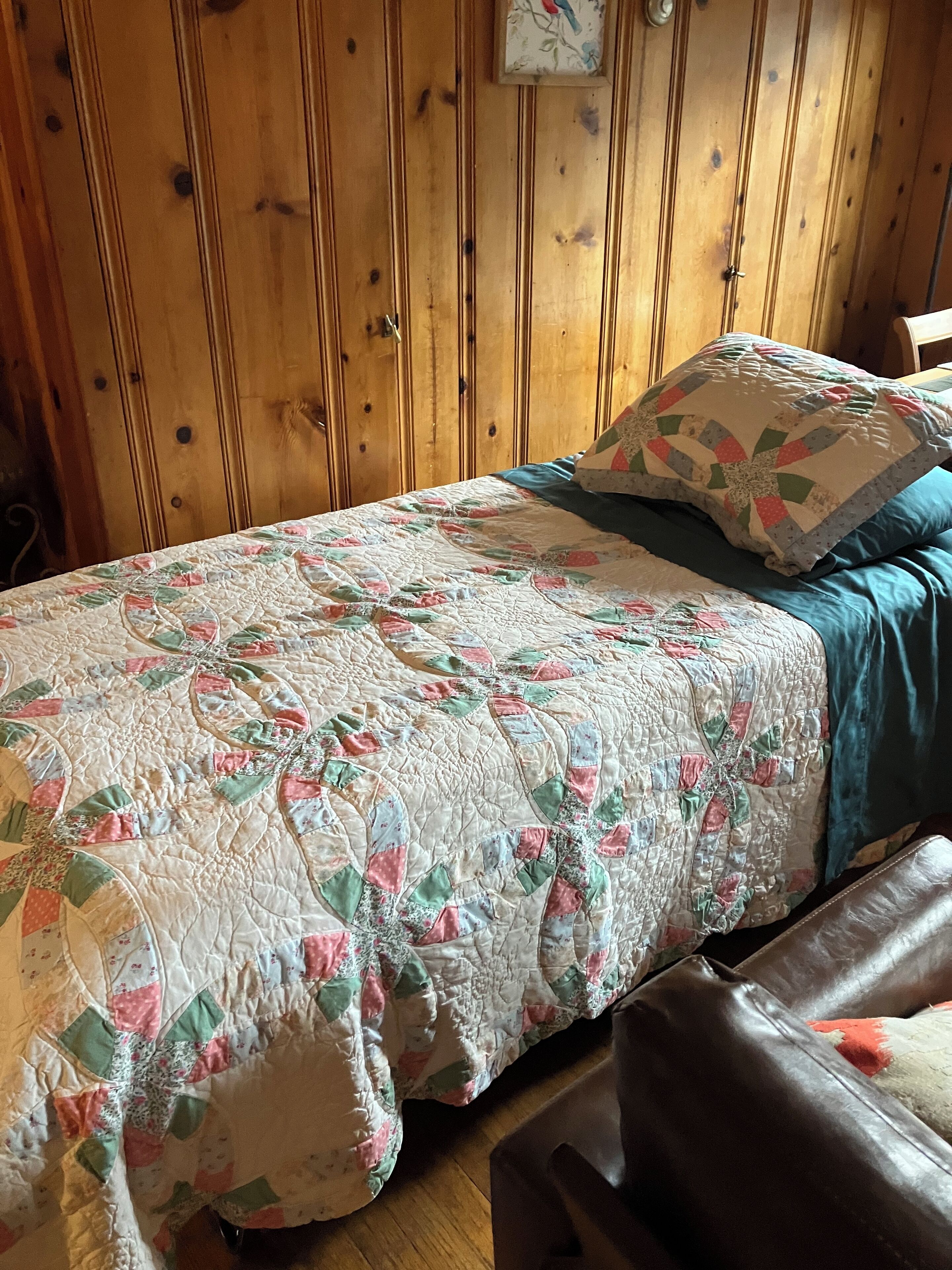 Una habitación con paneles de madera, una cama con colcha floral y una almohada azul.