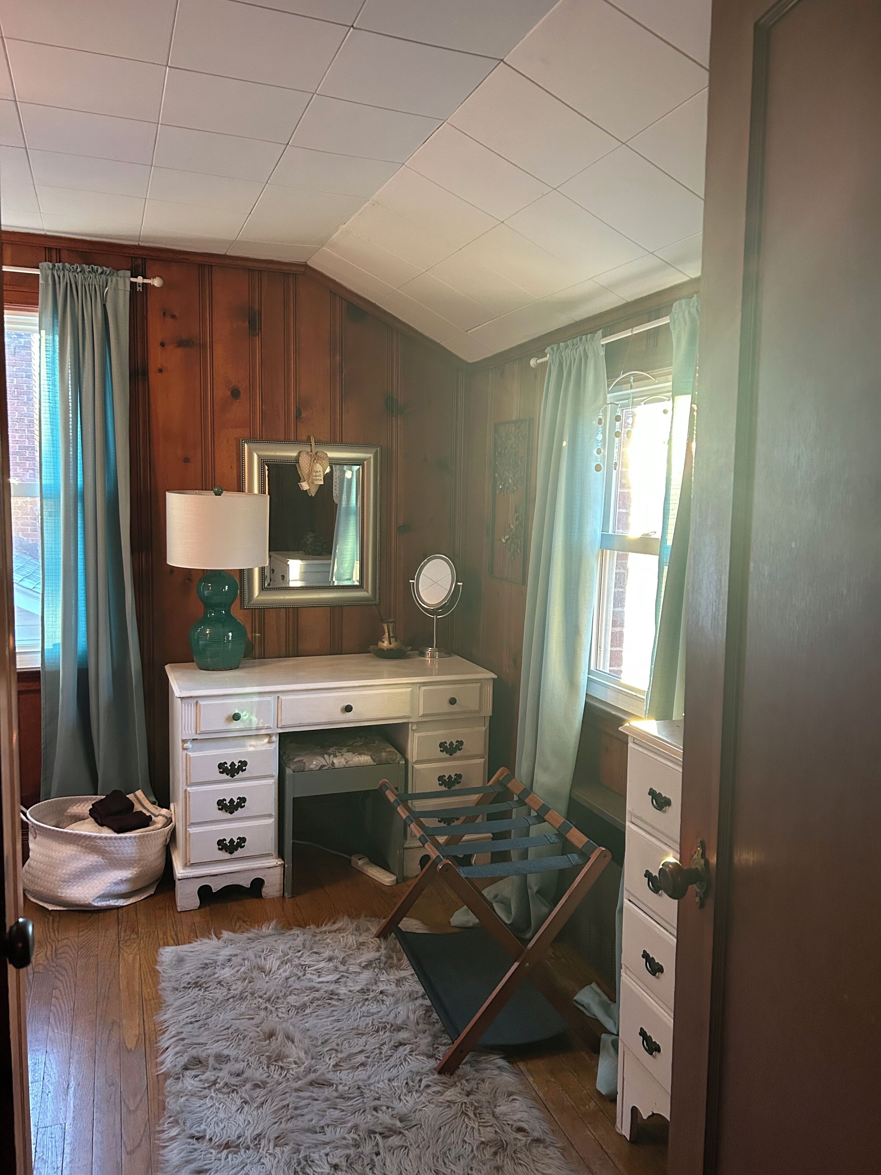 Un dormitorio con un aparador de madera, un espejo, una alfombra mullida y una ventana con cortinas.