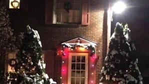 Una casa de ladrillo con un jardín delantero cubierto de nieve, una entrada iluminada y decoraciones navideñas.