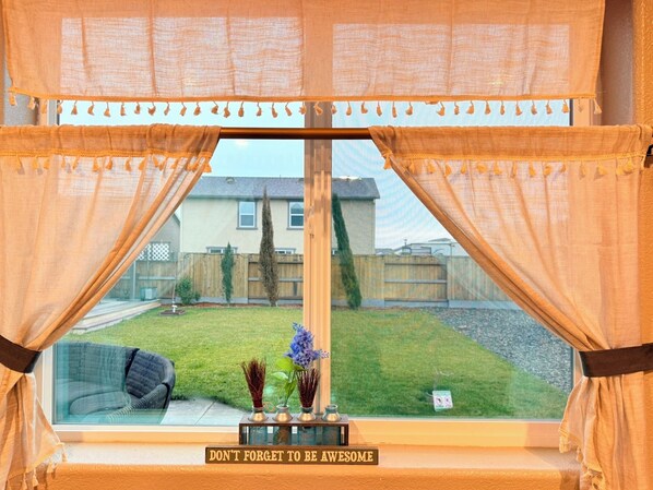 A window with curtains, a view of a backyard, and a sign that says "DON'T FORGET TO BE AWESOME".