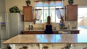 A kitchen with a central island, wooden bar stools, a refrigerator, and a window with curtains.