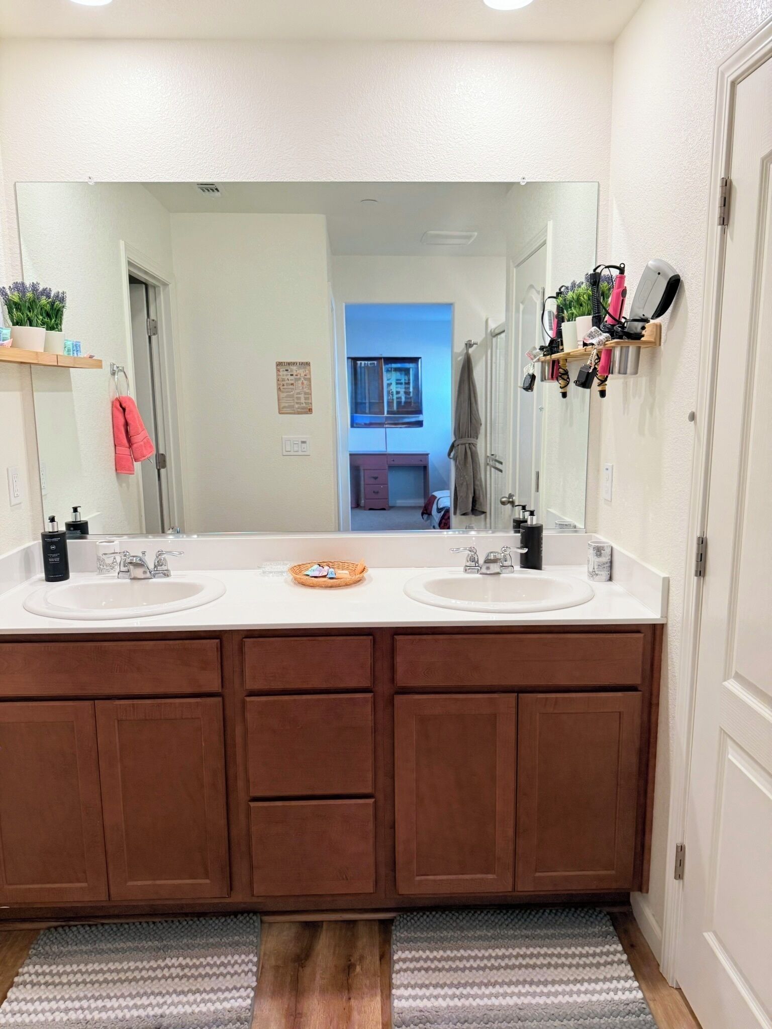 Un baño con dos lavamanos, armarios de madera, un espejo grande y un perchero para toallas.