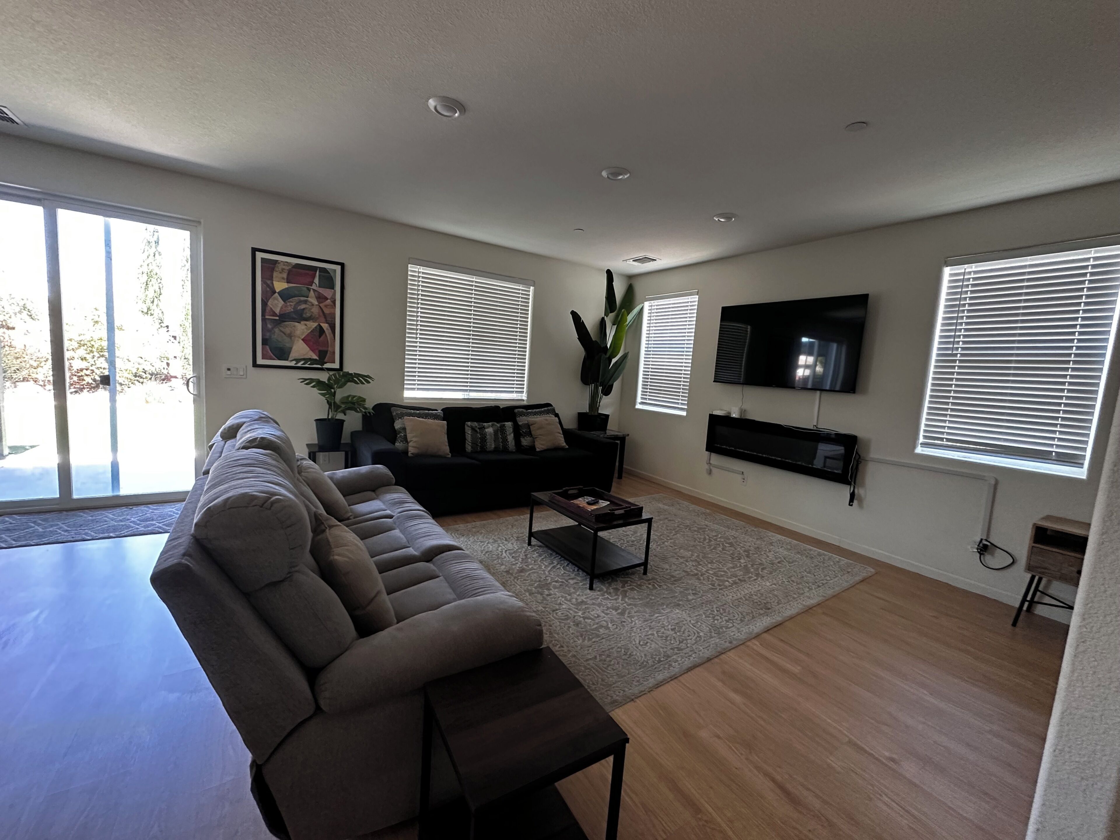 A modern living room with a sectional sofa, a coffee table, and a flat-screen TV mounted on the wall.