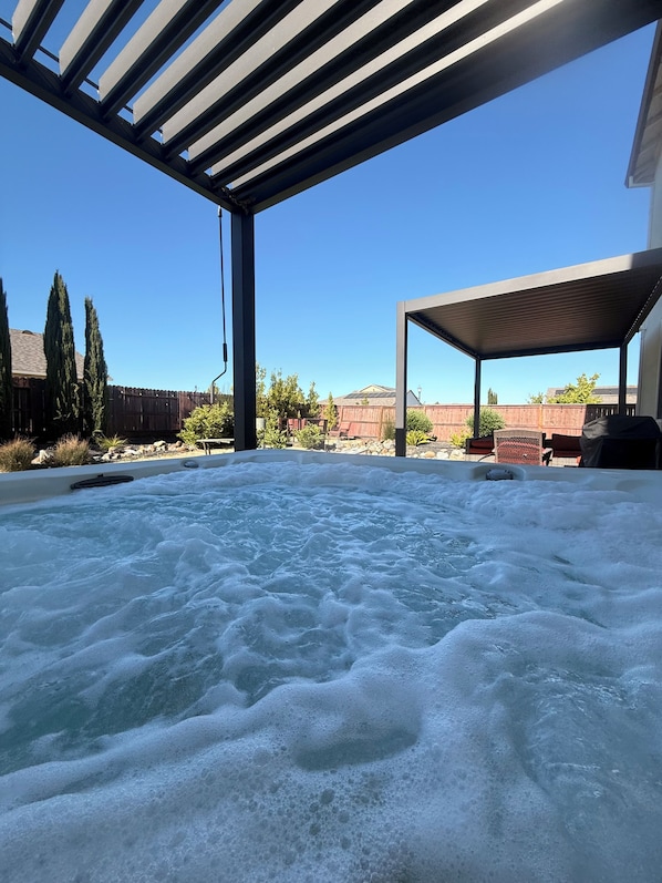 A hot tub under a covered patio with a clear view of a wooden fence and trees in the background.
